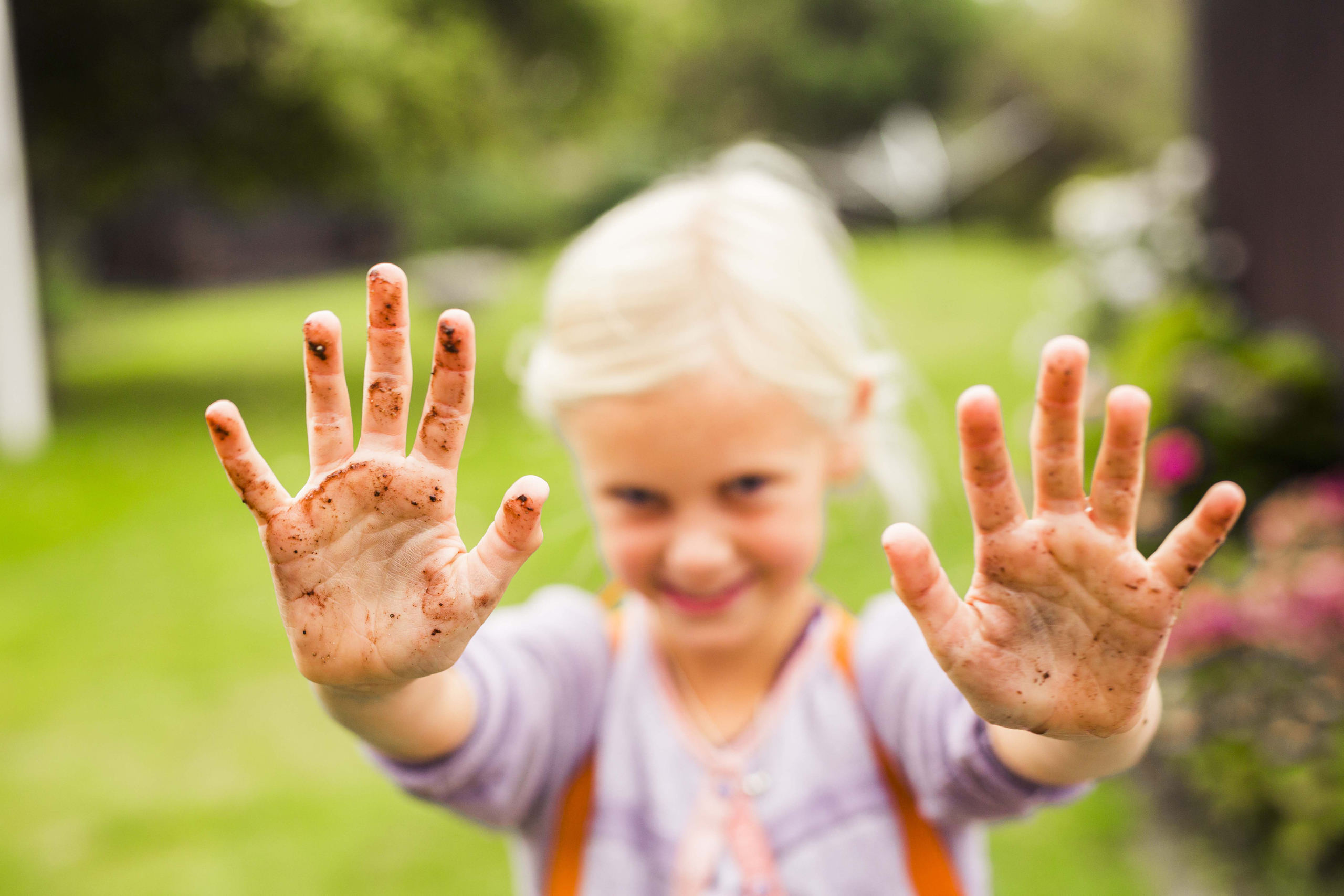 portrait-of-girl-showing-her-dirty-hands-in-garden-BJV6TAL